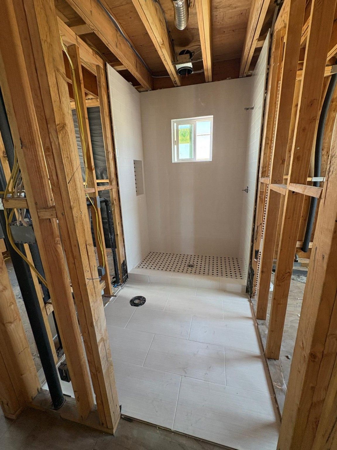 Bathroom under construction with surrounding exposed framing and a tiled shower