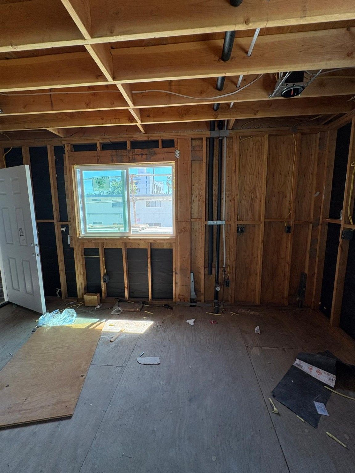 ADU interior with exposed wood framing, window opening and plumbing rough-in