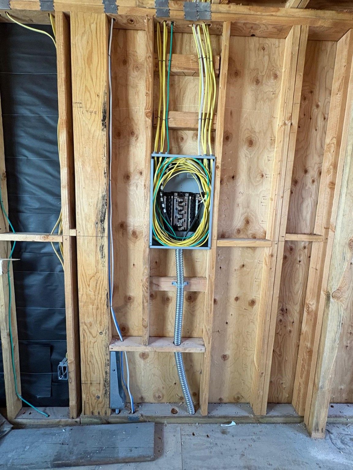 Close view of electrical wiring and a panel between exposed wall studs