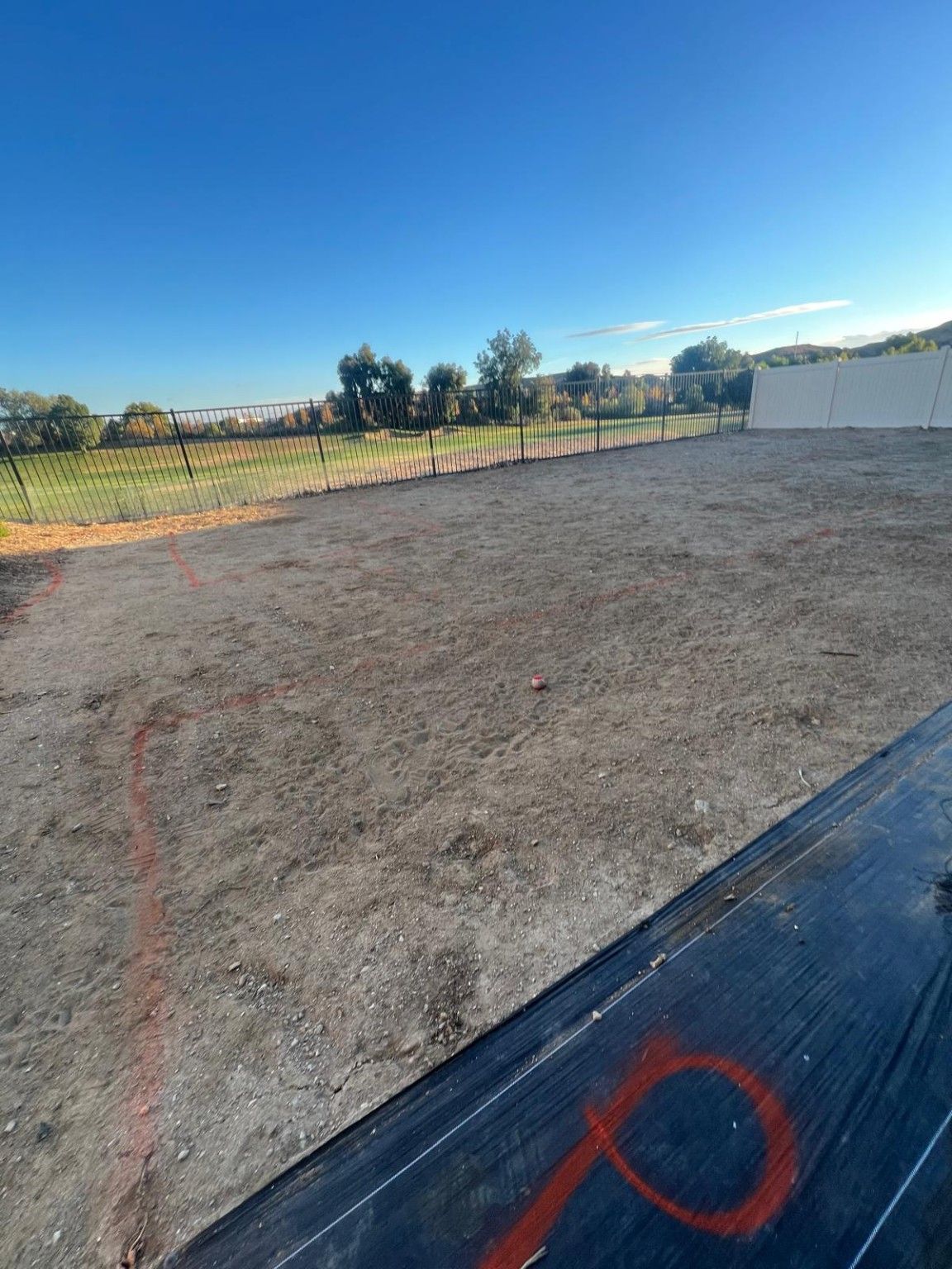 Red layout markings across bare soil, with black sheeting in the foreground and metal fencing beyond