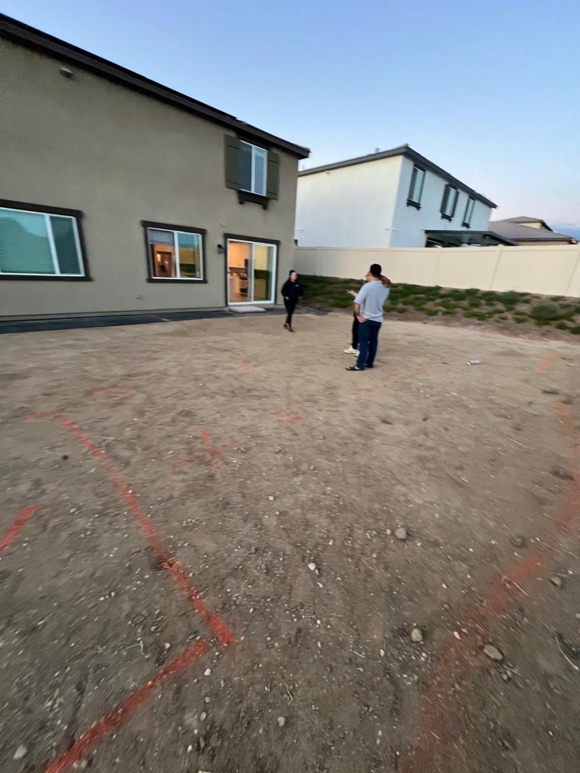 Bare backyard with red layout lines and people standing near the house’s sliding glass door
