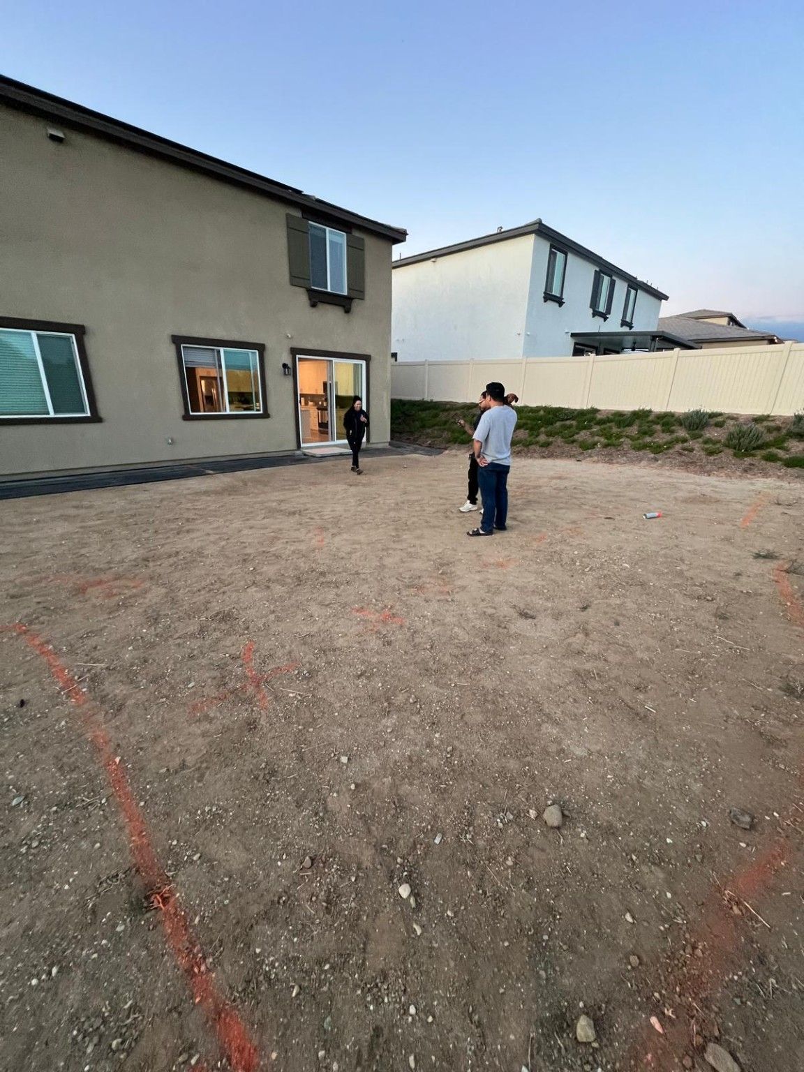Bare soil beside the rear entry, with people in the yard and a planted strip along the white fence