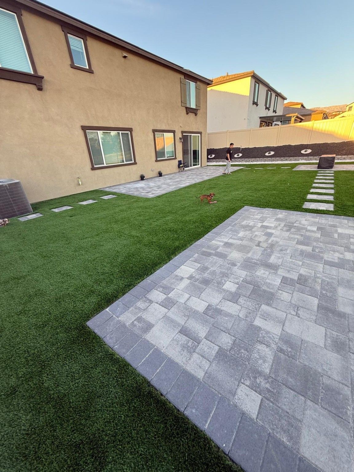Artificial turf with a stepping-stone path beside a paver patio