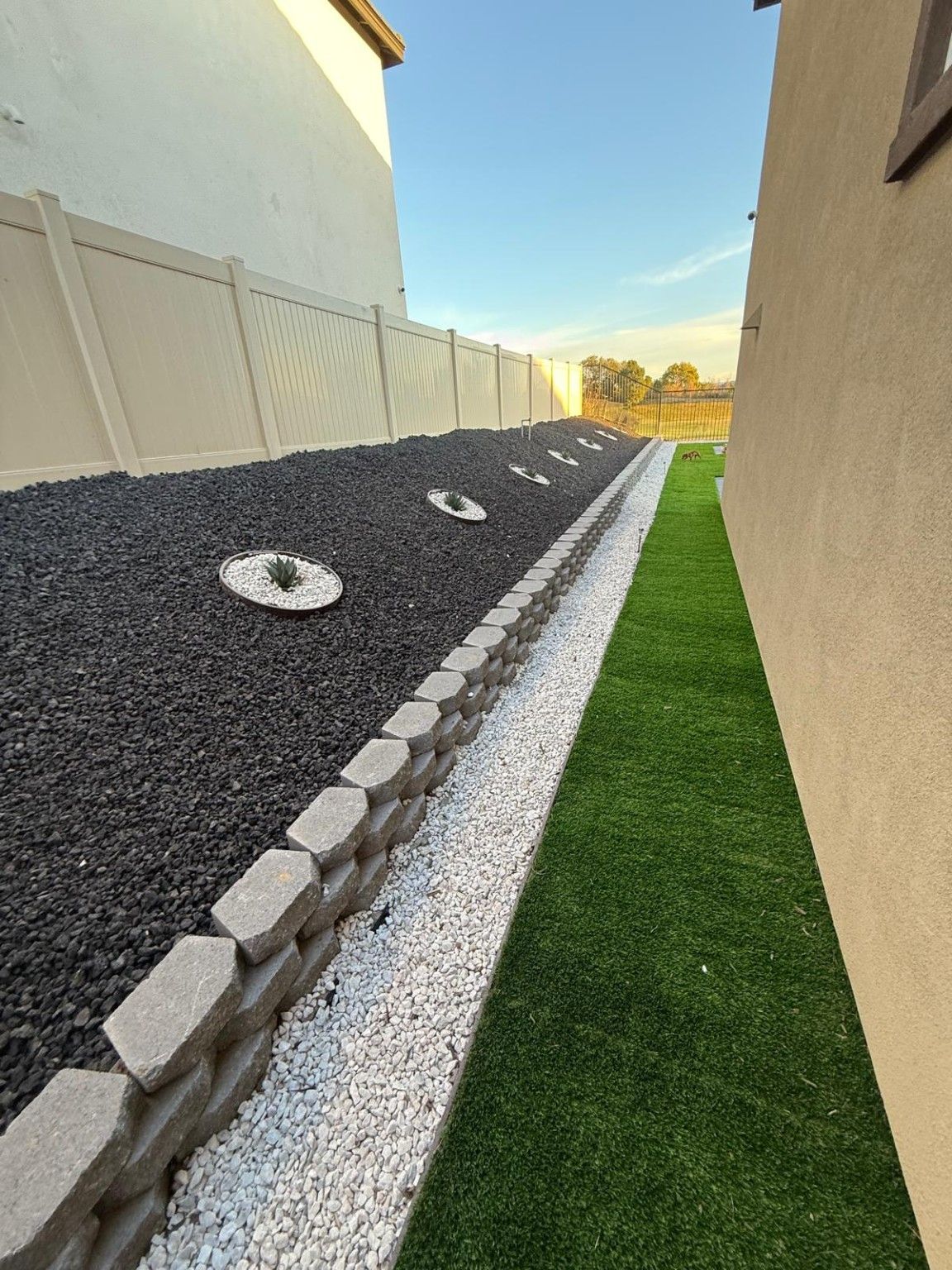 Raised block planter with dark decorative rock and circular light-colored accents beside turf