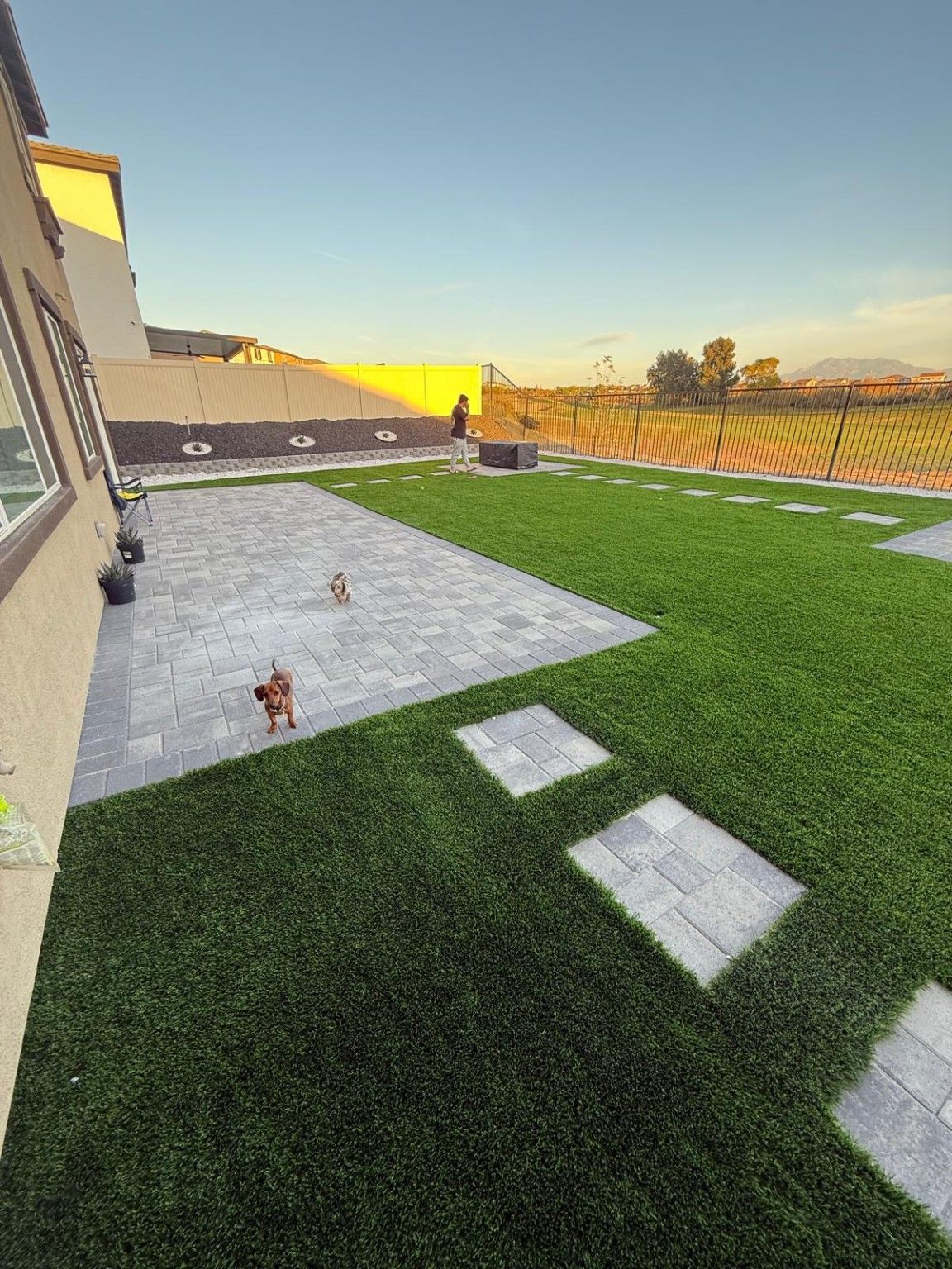 Backyard with gray pavers, green artificial turf, stepping stones and a planted border