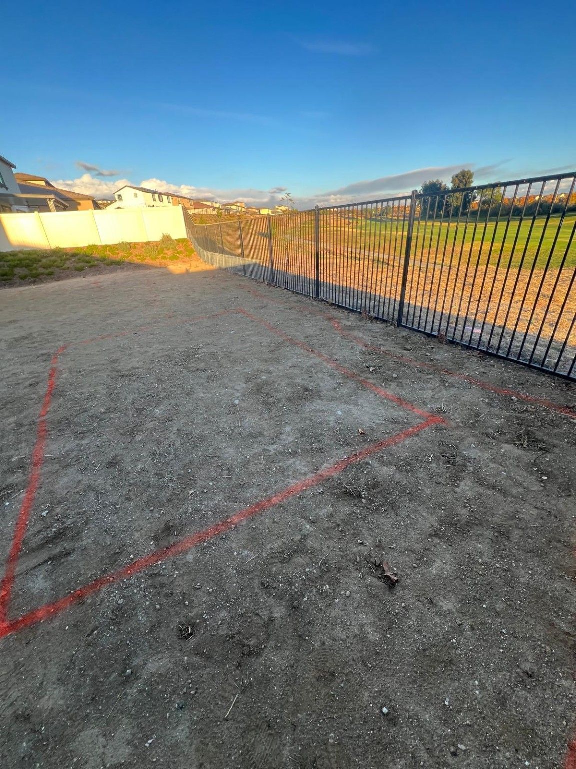 Bare yard with red layout markings beside boundary fencing