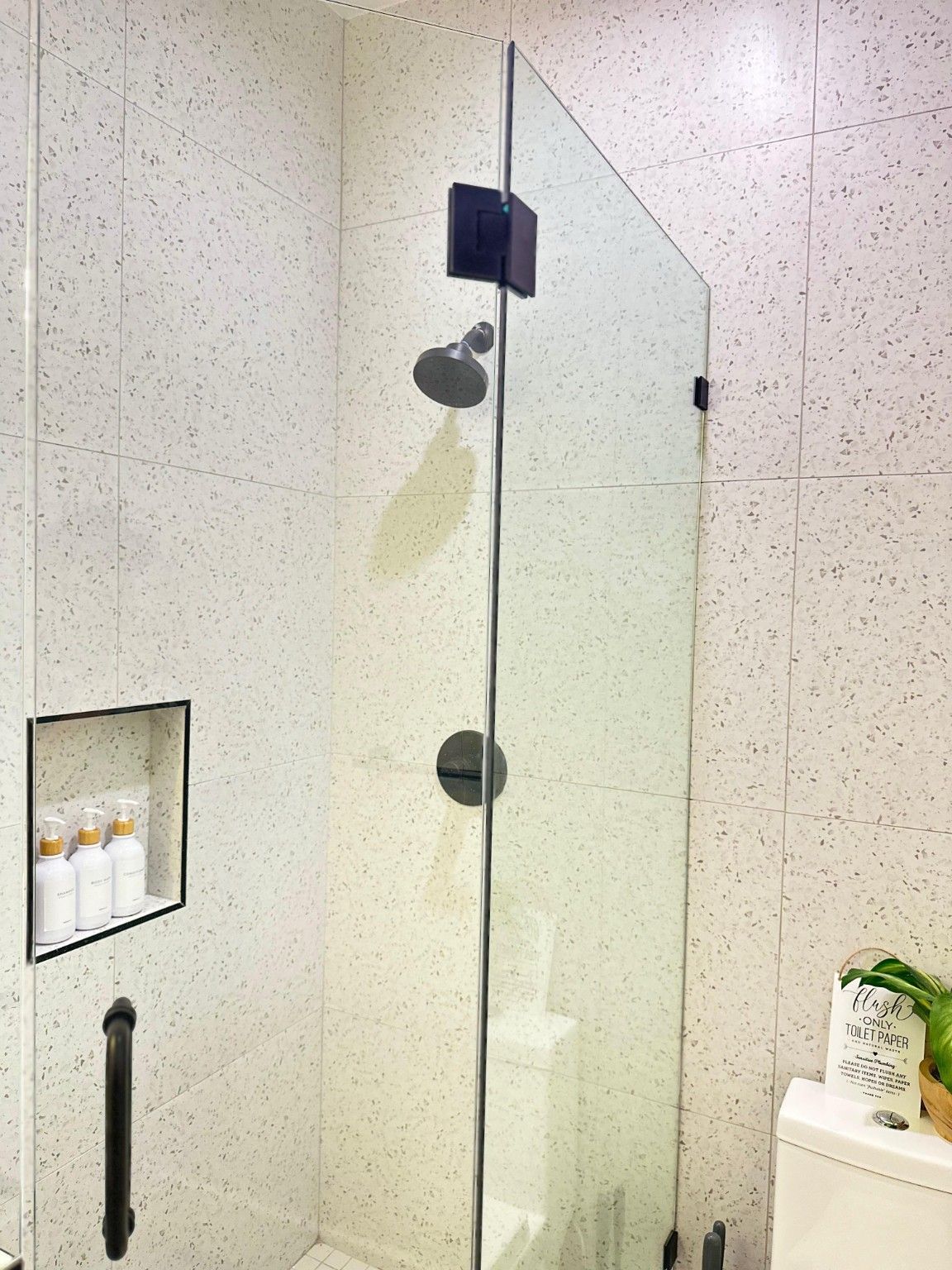 Glass shower enclosure with pale tile, a recessed niche and dark shower fixtures