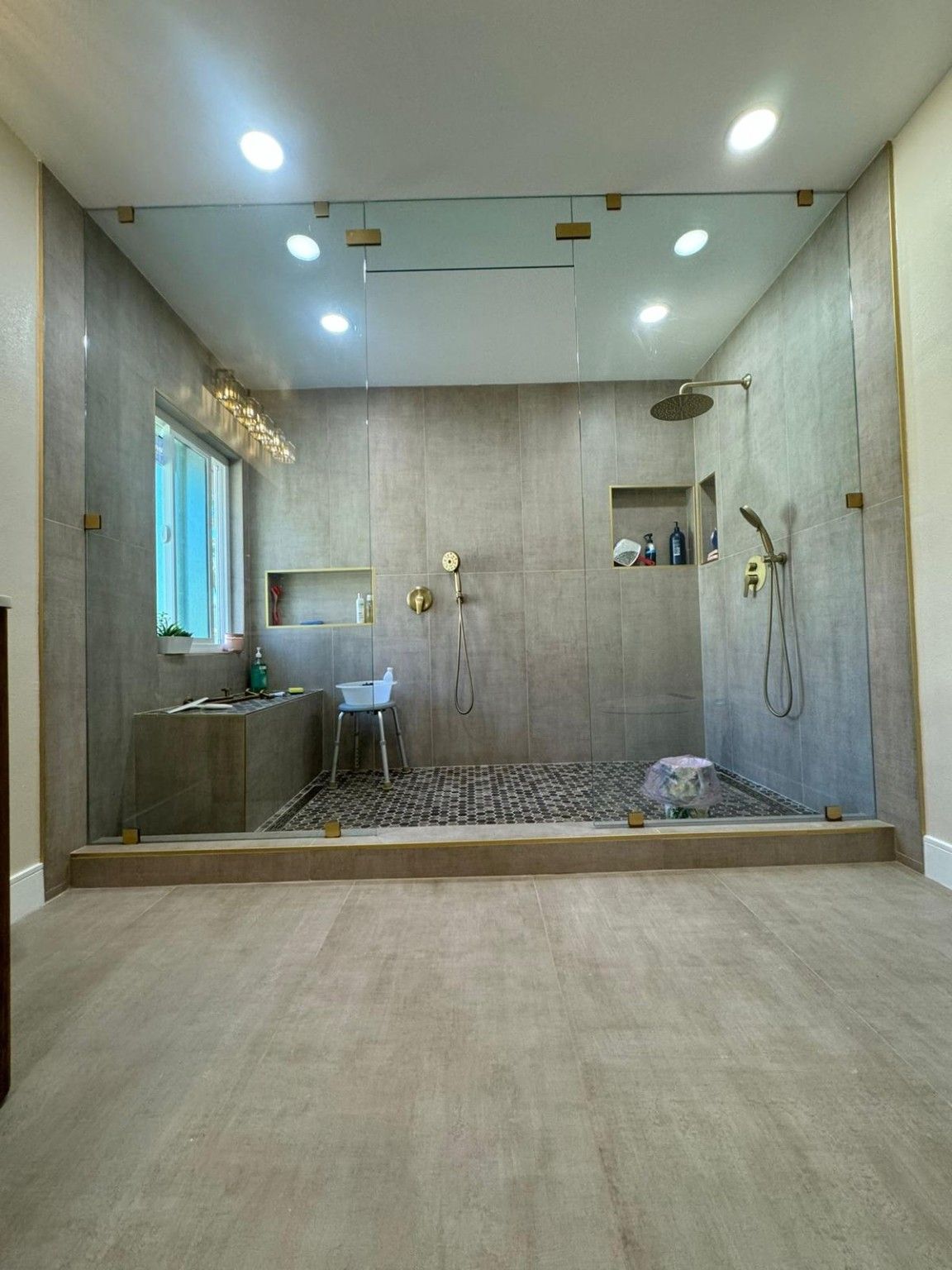 Glass shower enclosure with a raised edge, tile flooring and brass-tone shower fittings