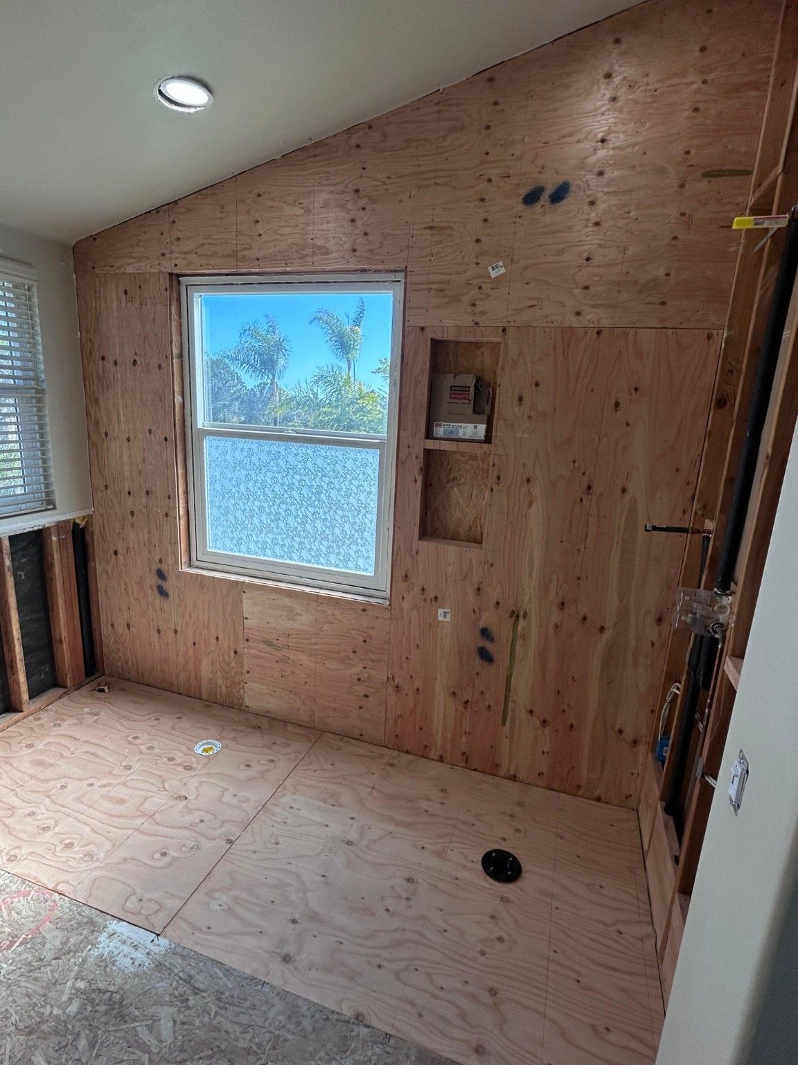 Bathroom wall and subfloor during construction, with plywood and recessed wall openings.