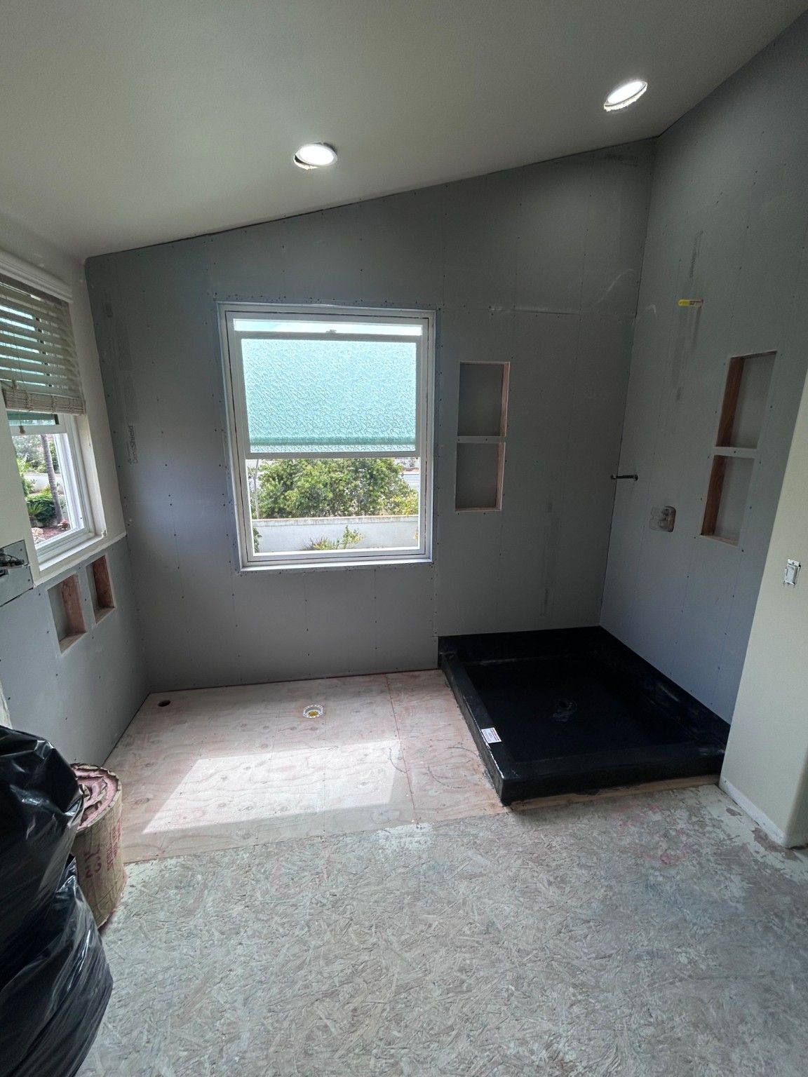 Bathroom during construction with wall panels, recessed niches and the shower base exposed.
