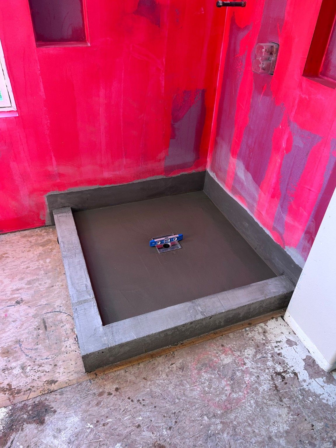 Shower base and drain during preparation, with a level resting at the drain.