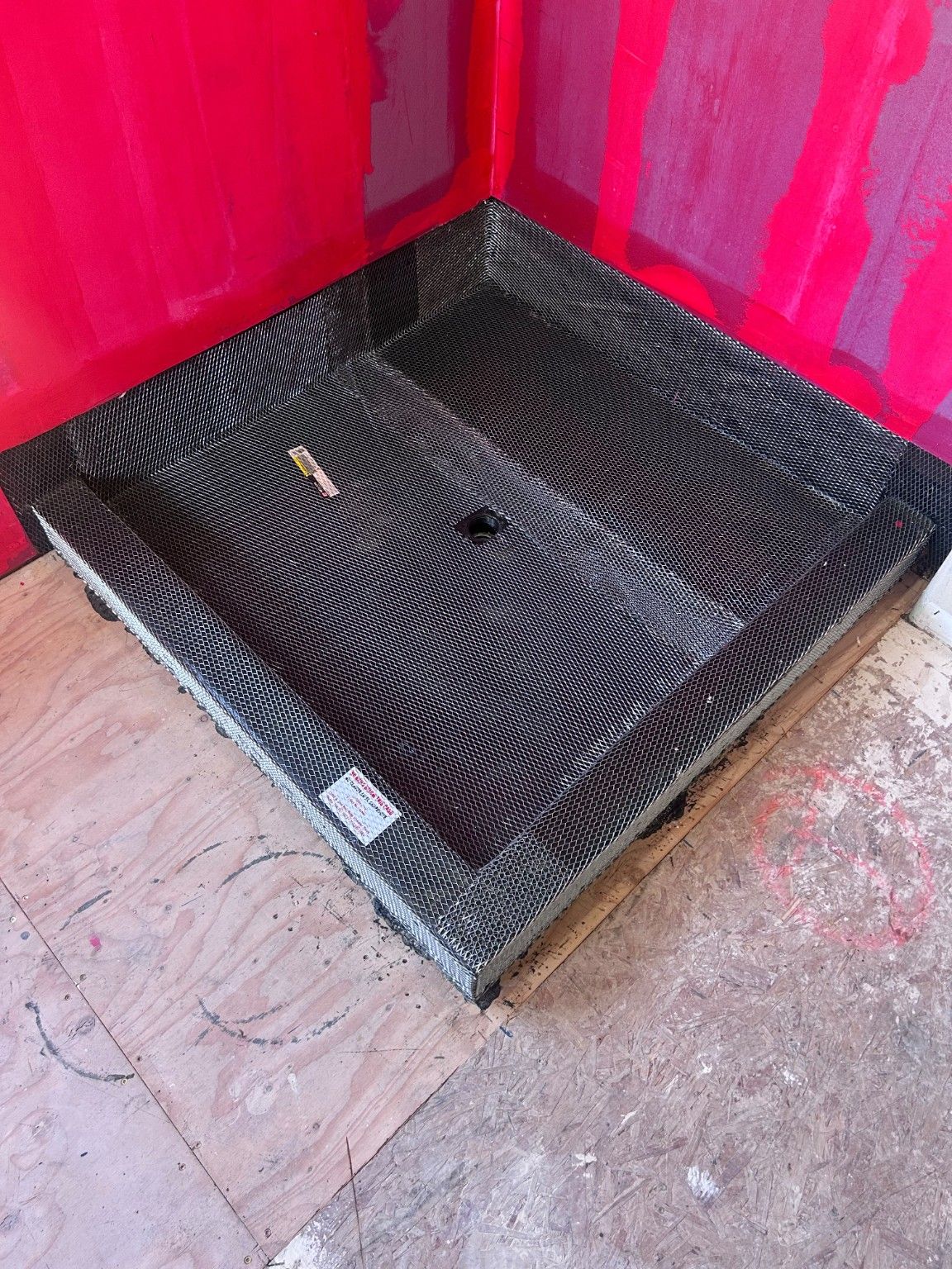 Close view of the shower base with mesh and a central drain opening during construction.