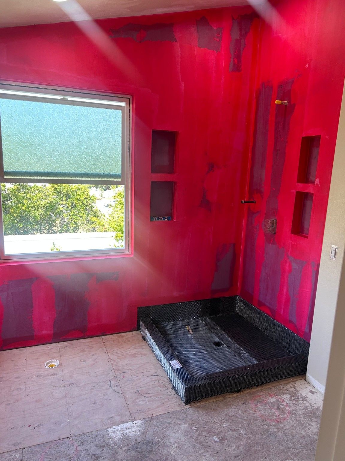 Shower base and red-coated walls during preparation, before the wall finish is installed.