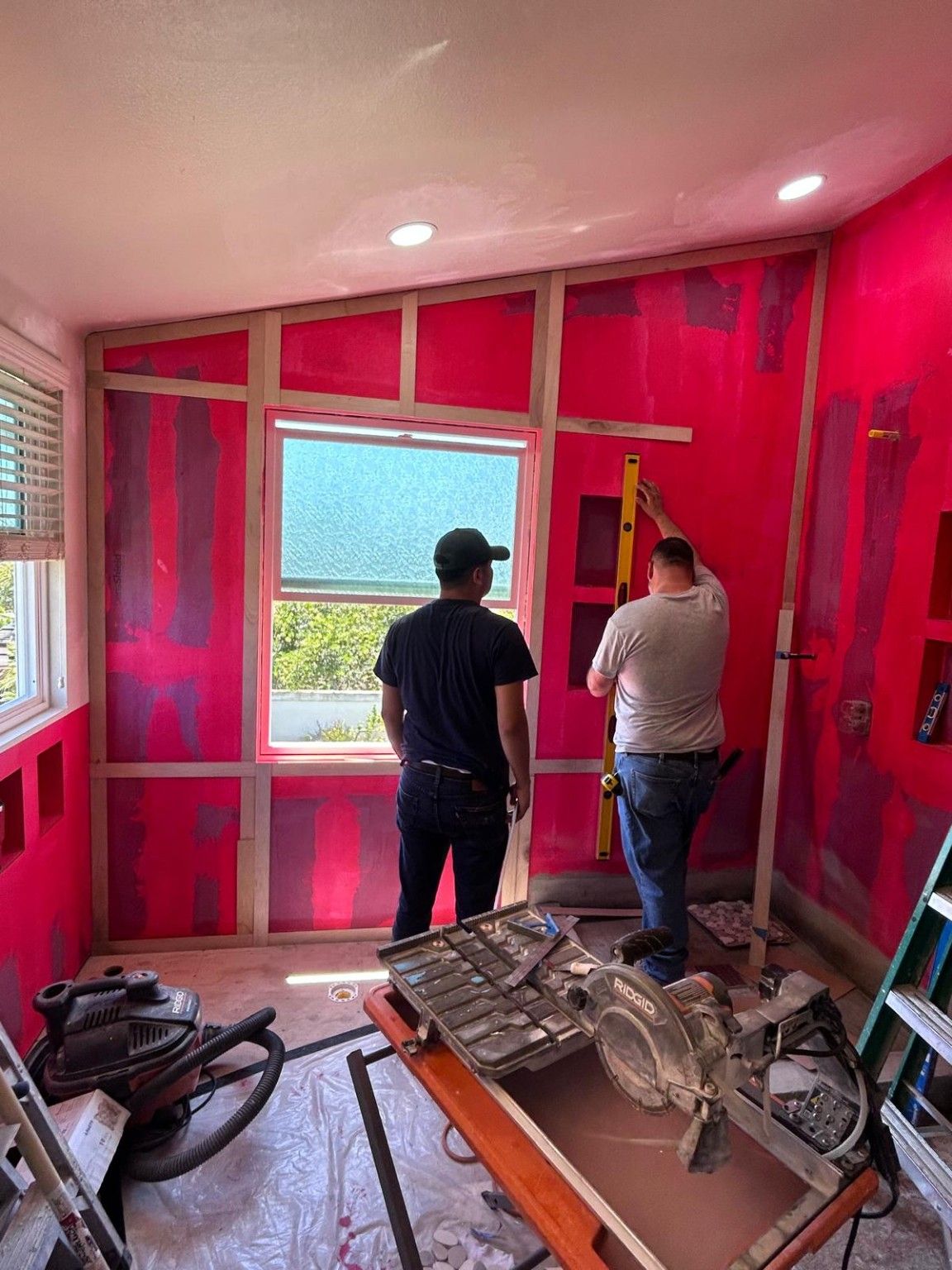 Two workers checking the layout beside the bathroom window during construction.