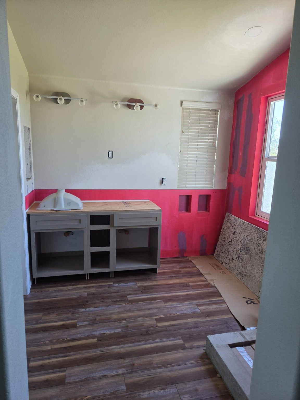 Gray vanity cabinet being installed beside the prepared bathroom walls.