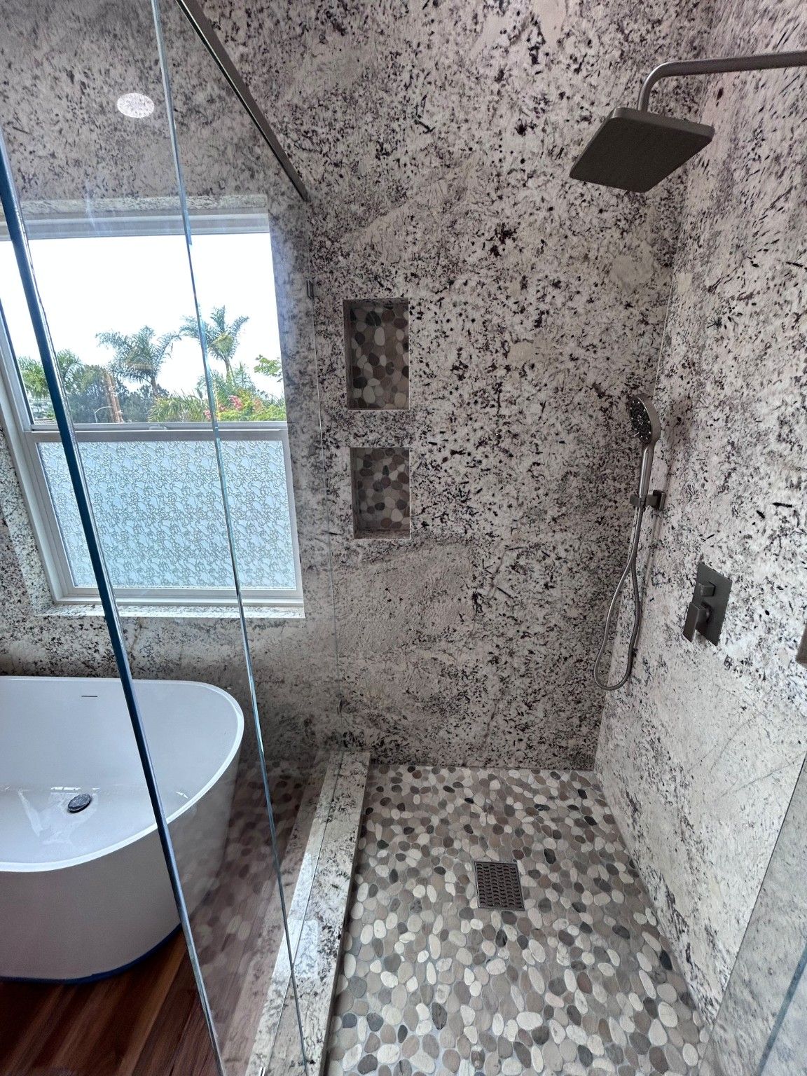 Rain shower head, handheld shower and recessed niches above a pebble-pattern shower floor.