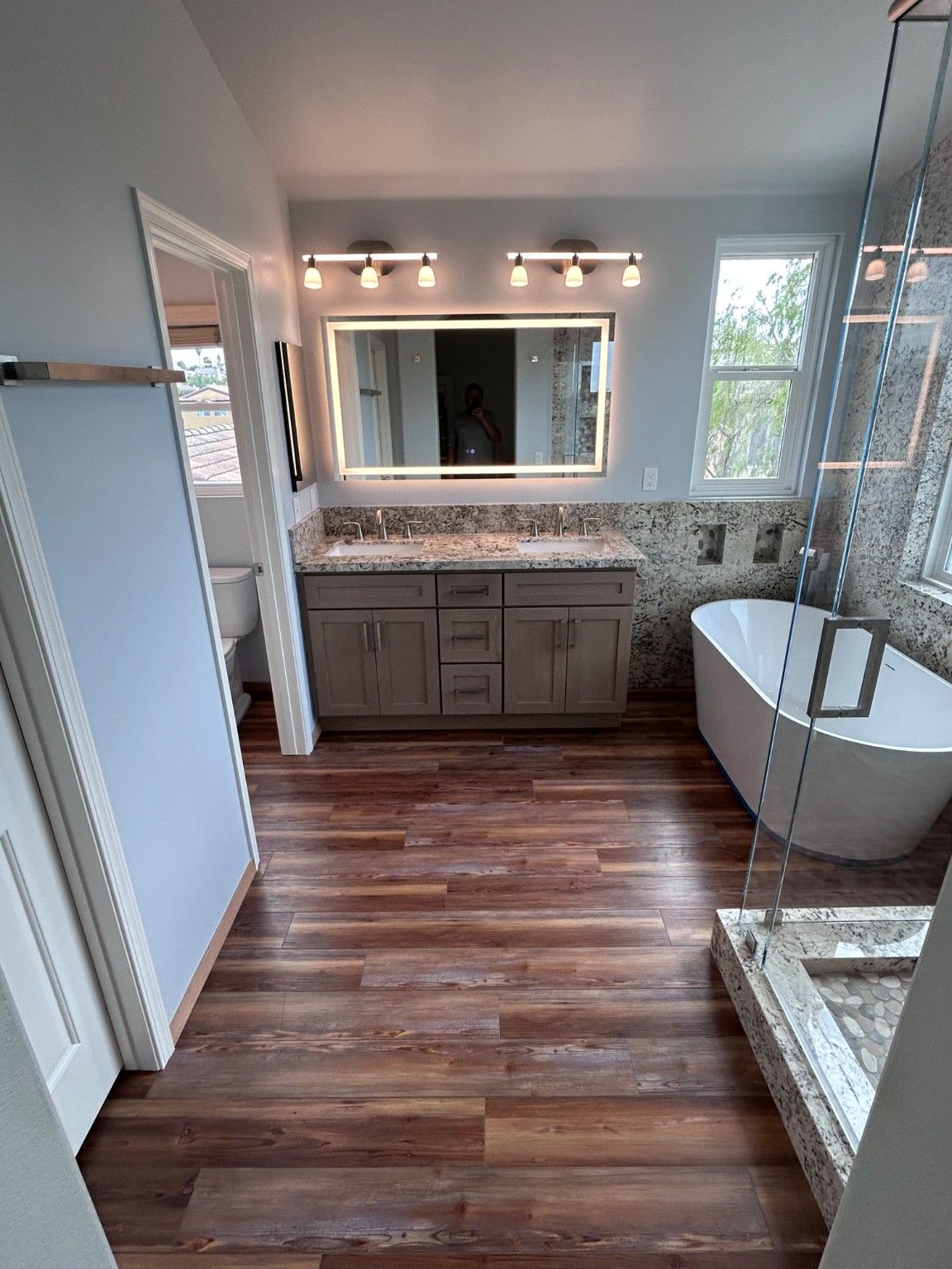 Gray double vanity and lighted mirror beside the freestanding tub and glass shower.