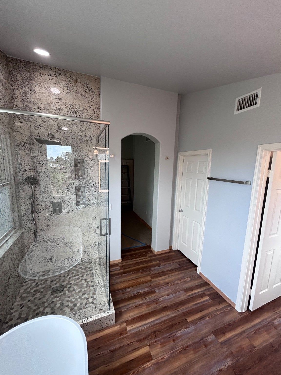 Glass shower enclosure, wood-look floor and bathroom doorways in the remodeled room.