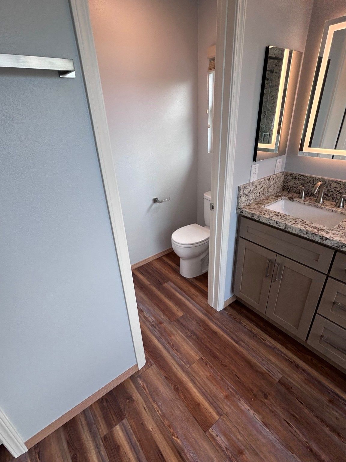 Updated gray vanity beside the separate toilet room and wood-look bathroom flooring.