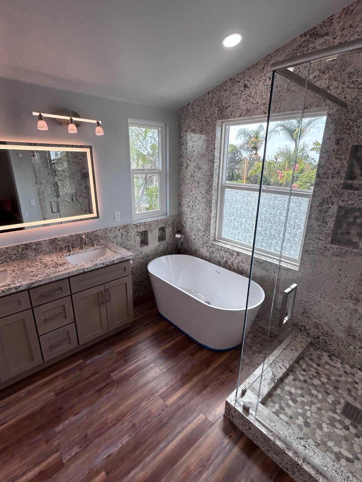 Finished bathroom view with a freestanding tub, gray vanity, lighted mirror and glass shower.