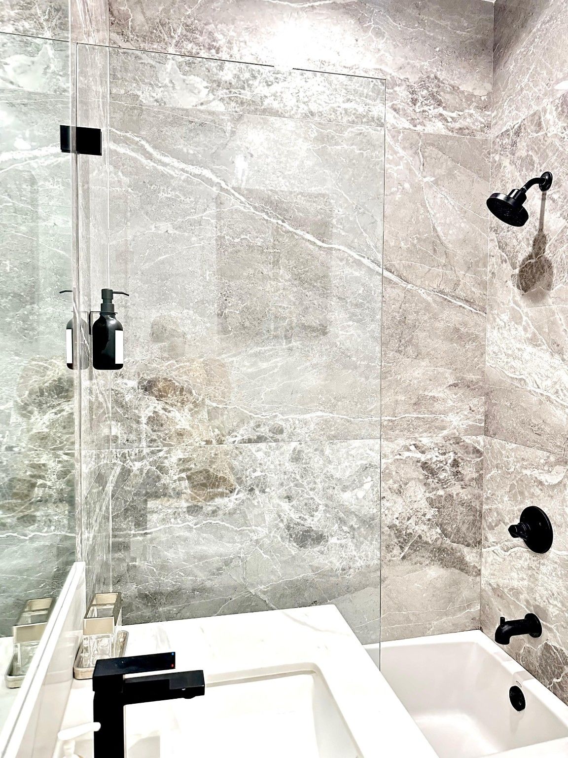 Bathroom with a white tub, gray veined wall tile and dark fixtures