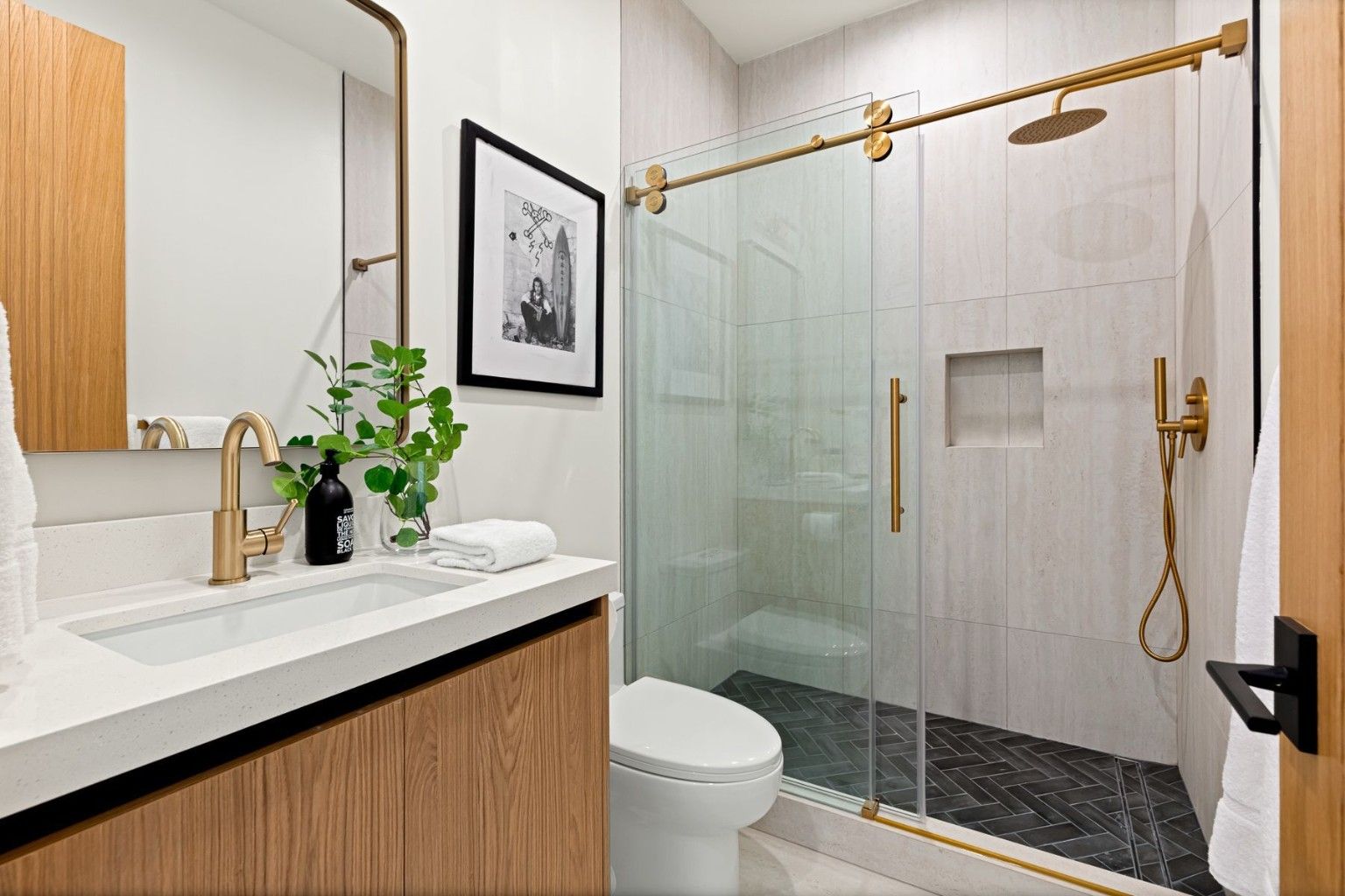 Bathroom with a warm wood vanity, pale tile, brass-tone fixtures and a glass shower