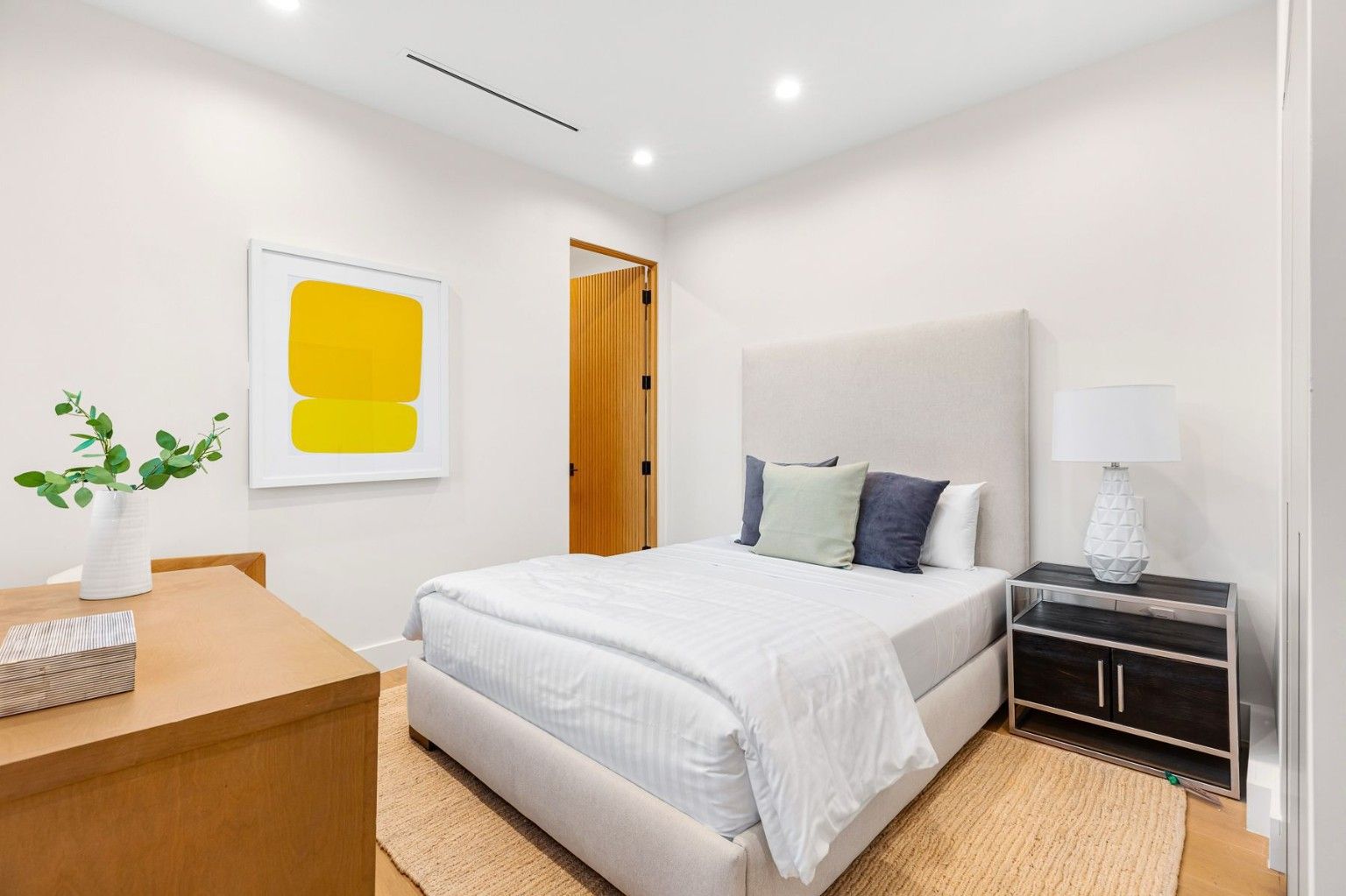 Bedroom with white walls, light wood flooring, a bed and simple furnishings