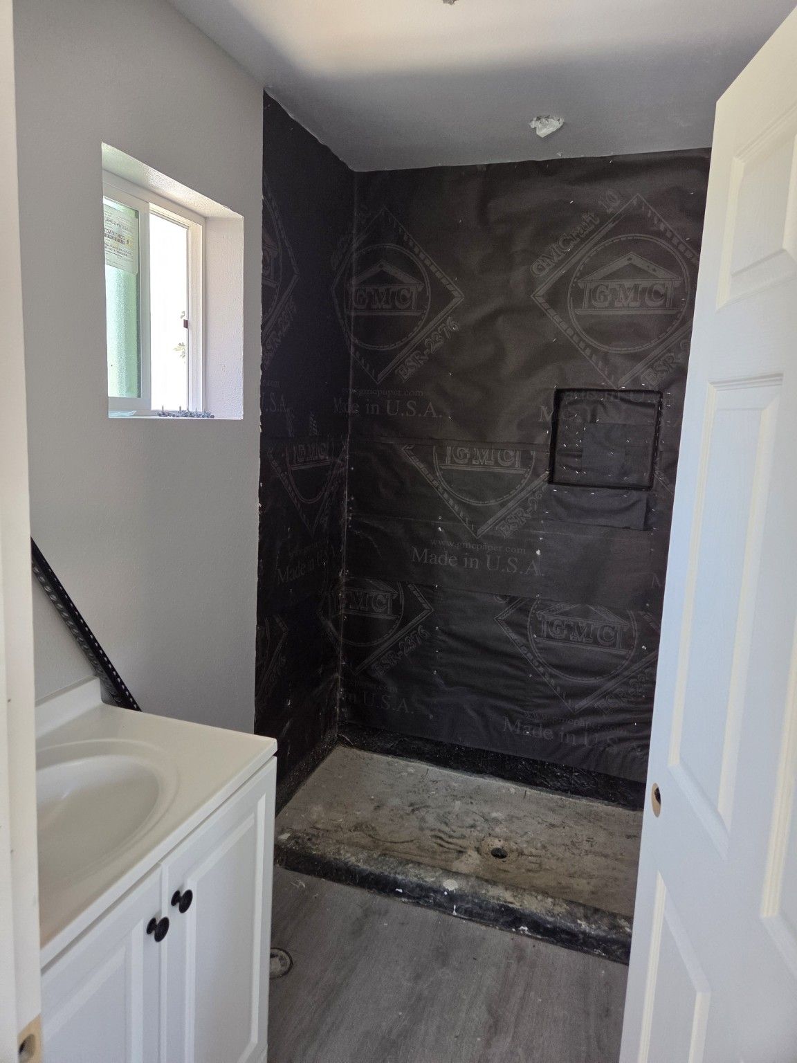 Bathroom with a white vanity and dark shower wall surfaces during finishing work