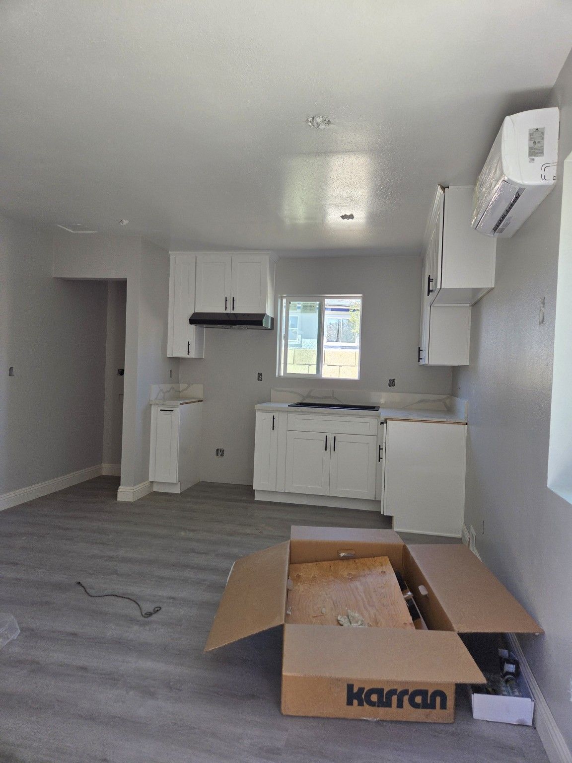 White kitchen cabinetry, a window and a wall-mounted indoor cooling unit during finishing work