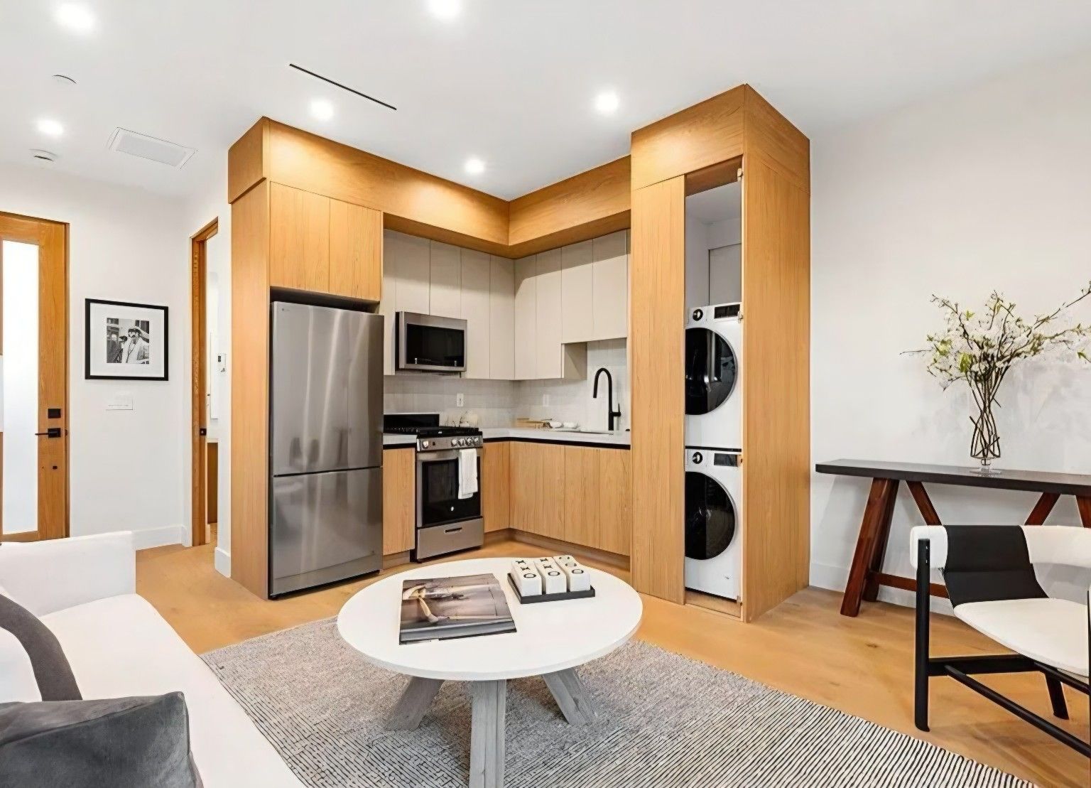 Open kitchen and sitting area with wood cabinetry, white upper cabinets and an integrated laundry space