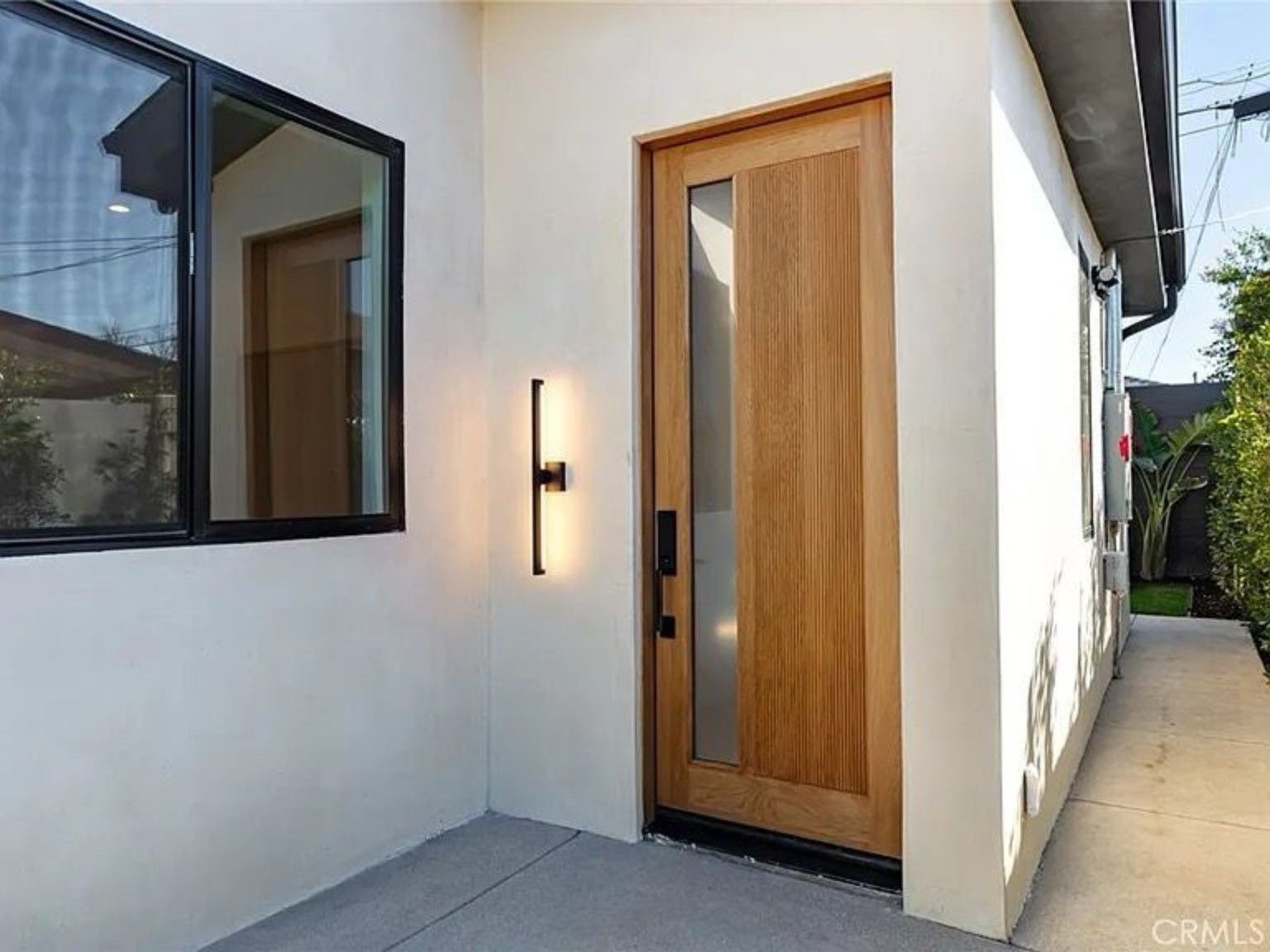 Exterior walkway beside a wood entry door, a black-framed window and a wall light