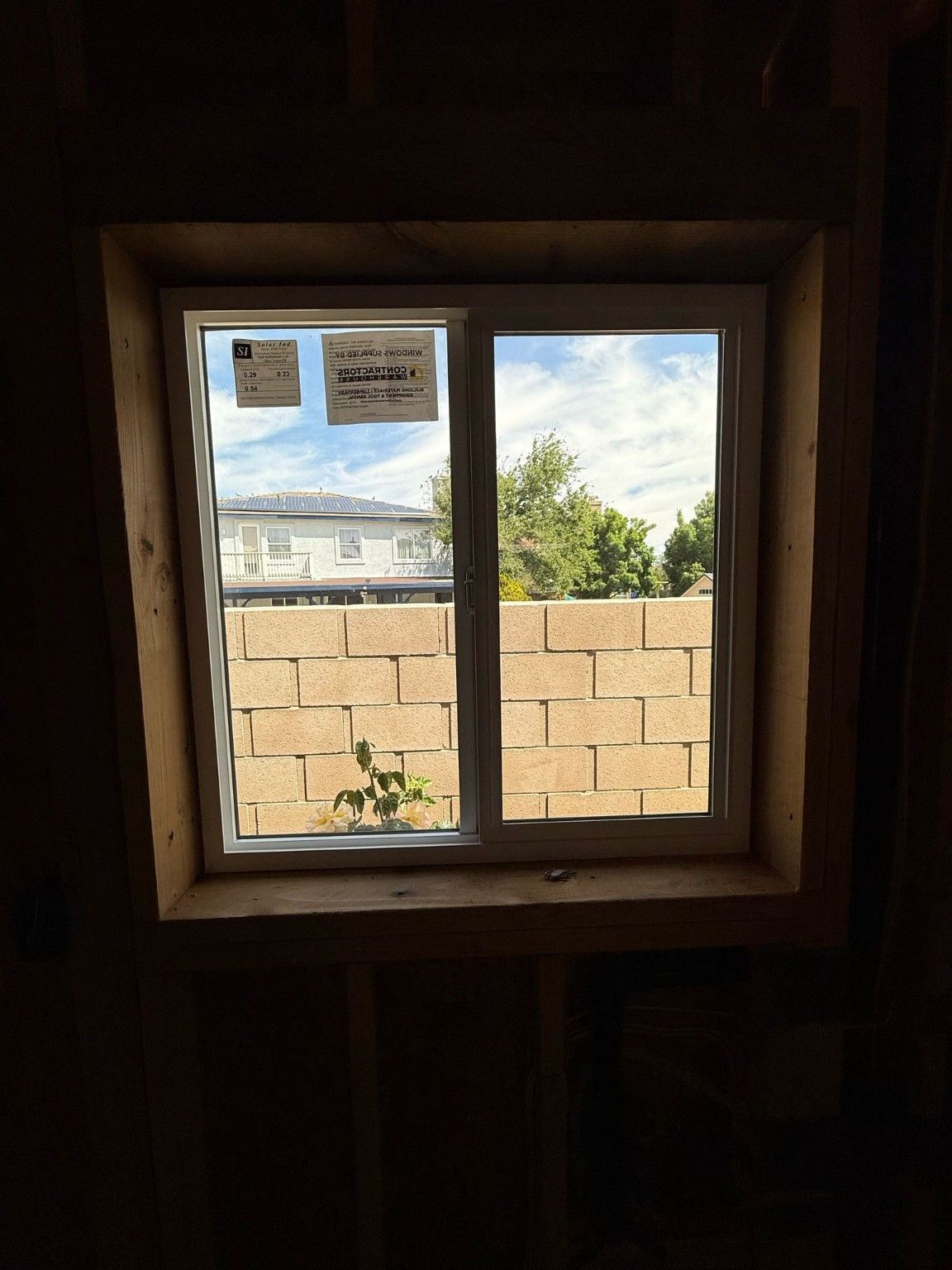 White-framed sliding window surrounded by exposed wood framing, with a block wall visible outside