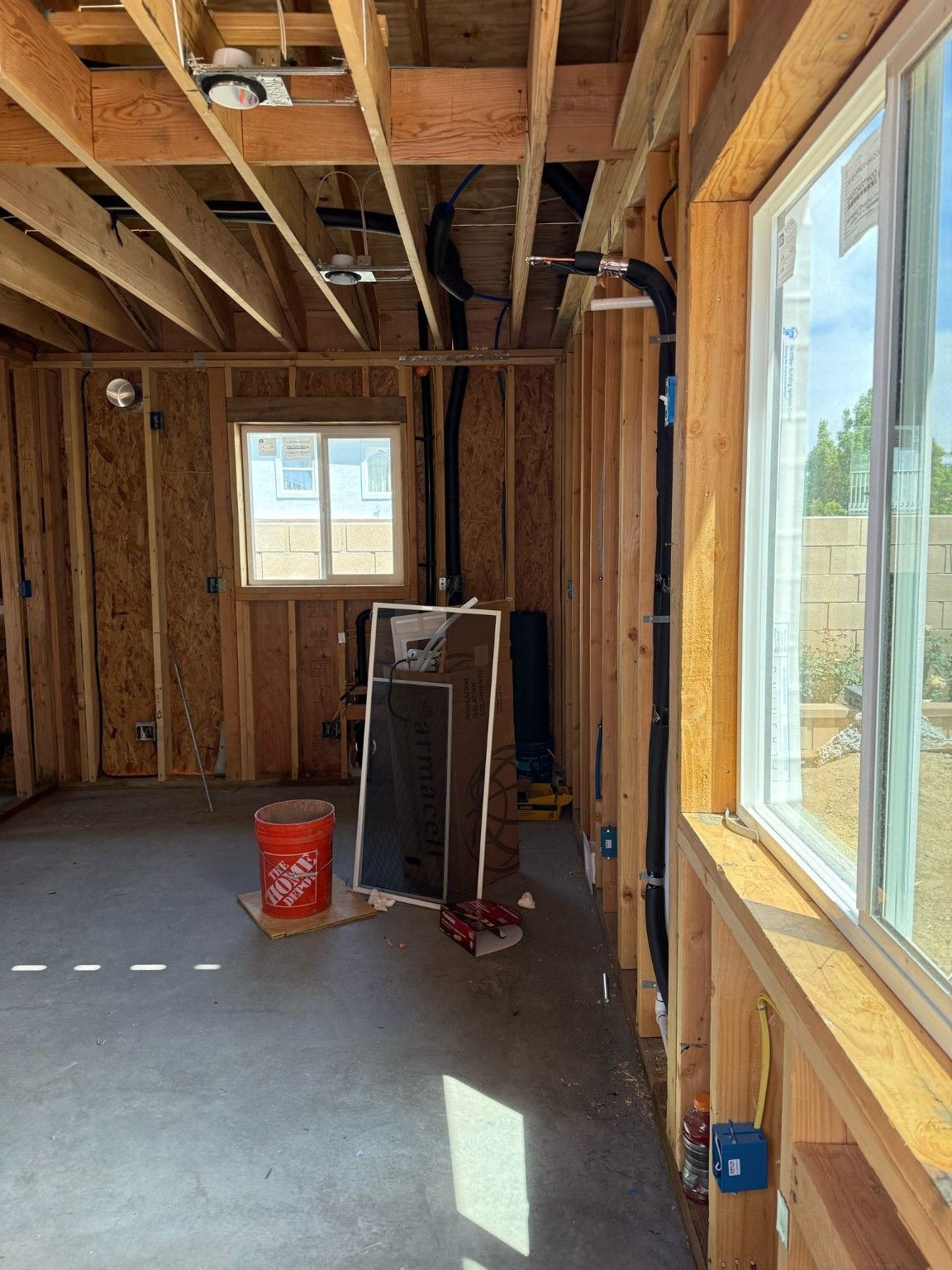 Exposed room framing beside a window with rough utility work