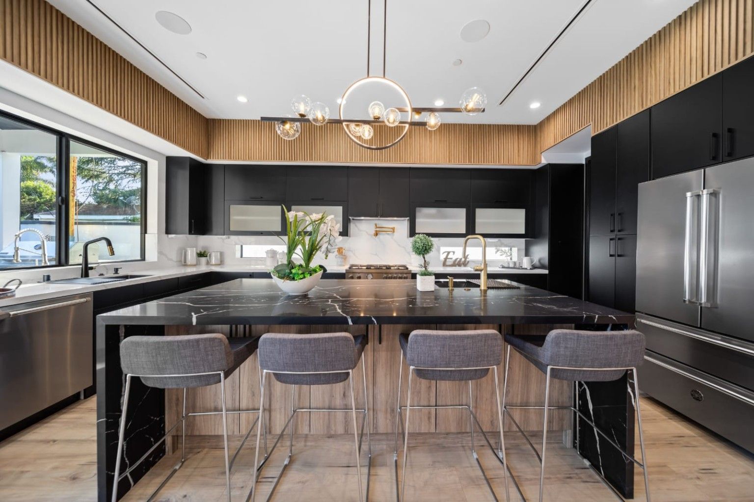 Kitchen with dark cabinetry, a wood island, seating and sculptural lighting