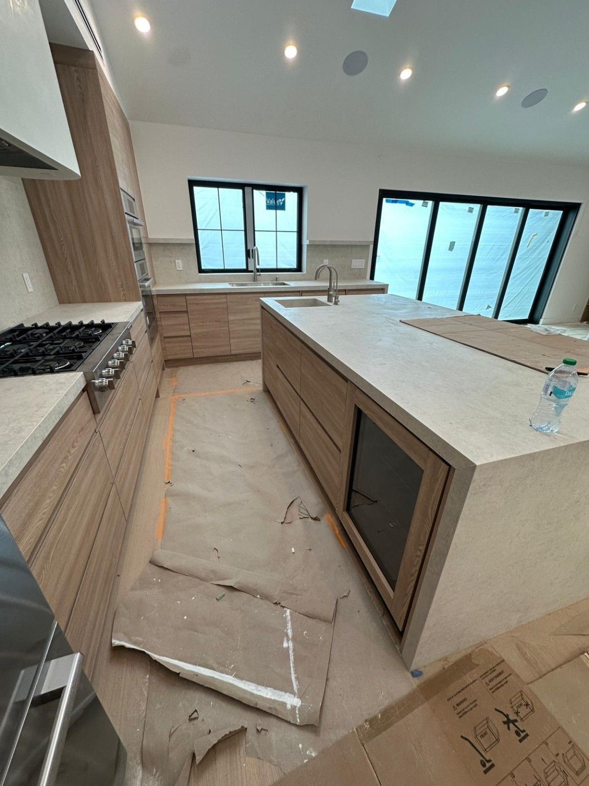 View along wood kitchen cabinets and an island while flooring is covered with protective material