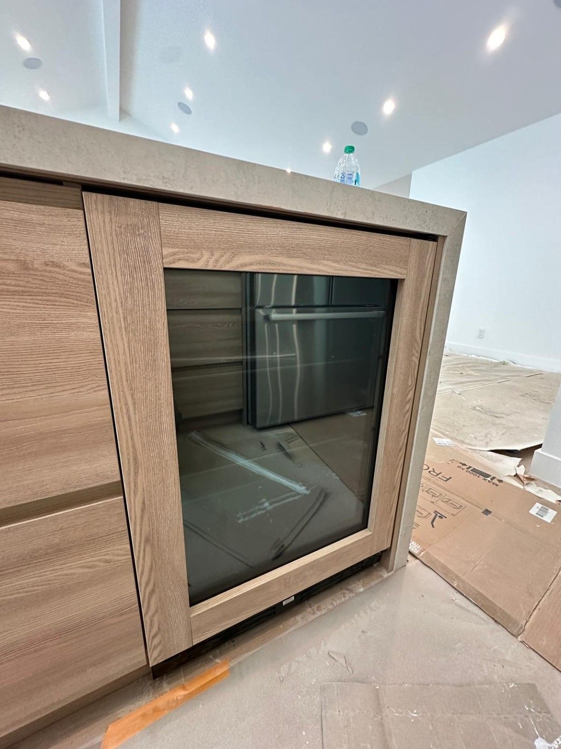 Close view of a glass-front appliance fitted into wood kitchen island cabinetry during work