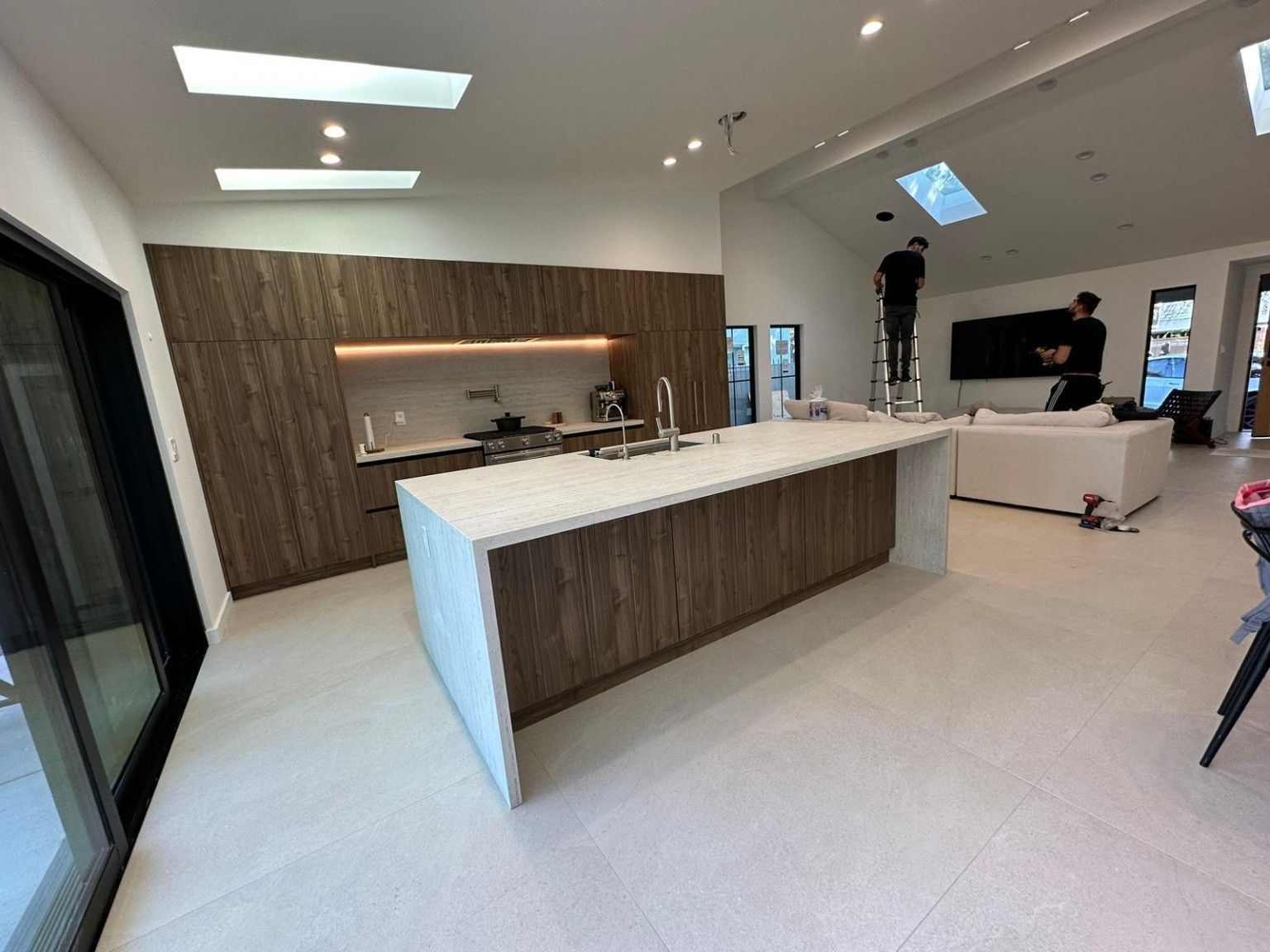 Wide view of a wood kitchen island with a light countertop and matching tall cabinets