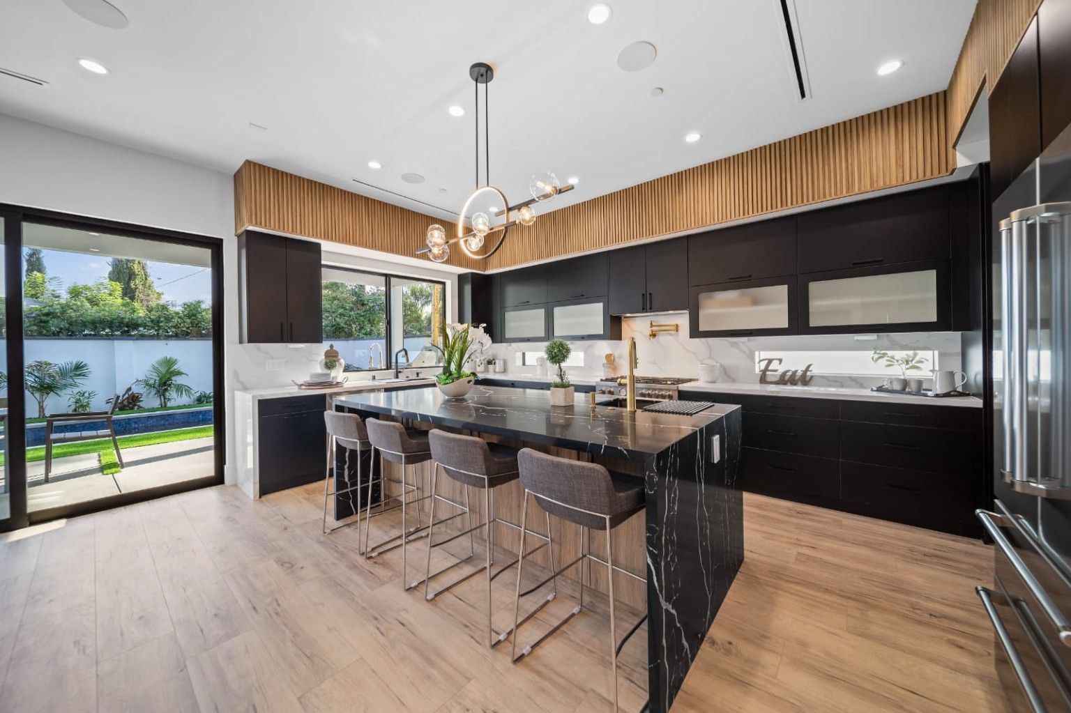 Finished kitchen with dark cabinetry, a waterfall island, warm wood detailing and sculptural lighting