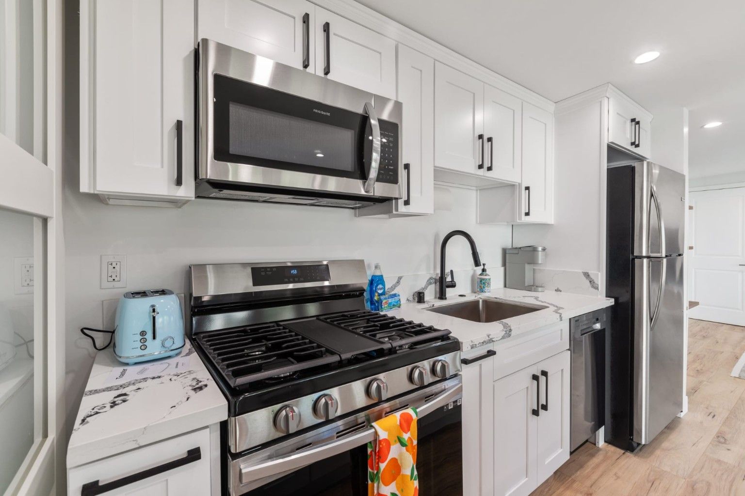 Kitchen range and microwave beside white cabinetry and a light veined countertop