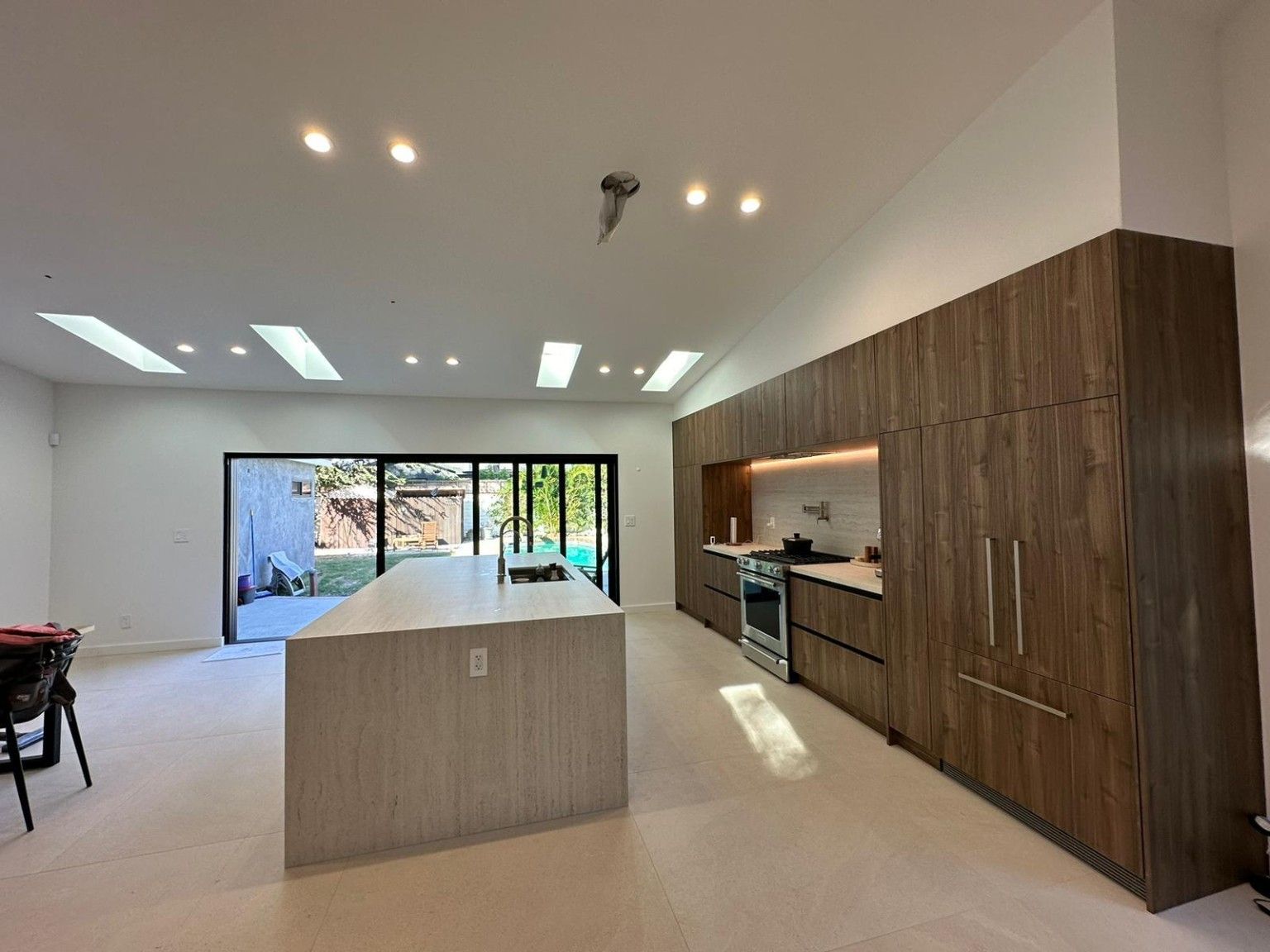 Wood kitchen cabinets and a long island beside glass doors leading outdoors