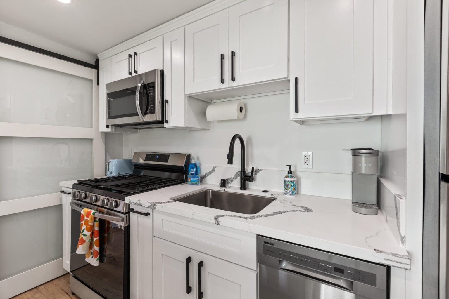 White kitchen cabinetry with dark handles, a sink, a range and a stainless dishwasher