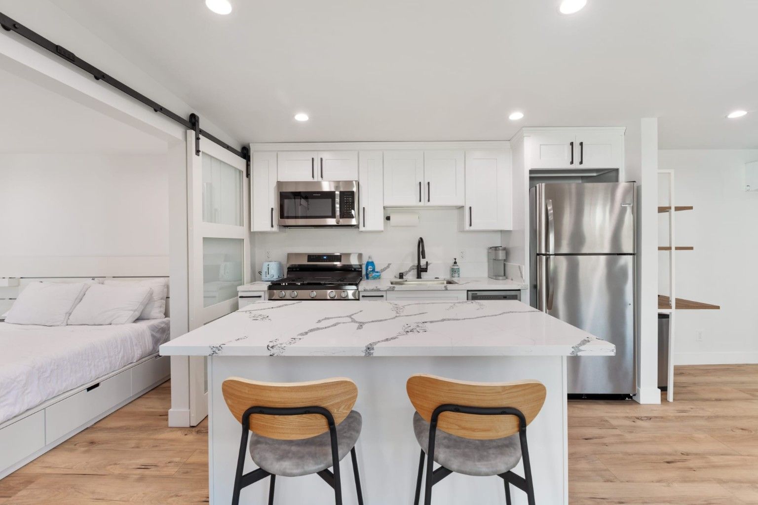 White kitchen with an island, two stools, stainless appliances and a sliding interior door