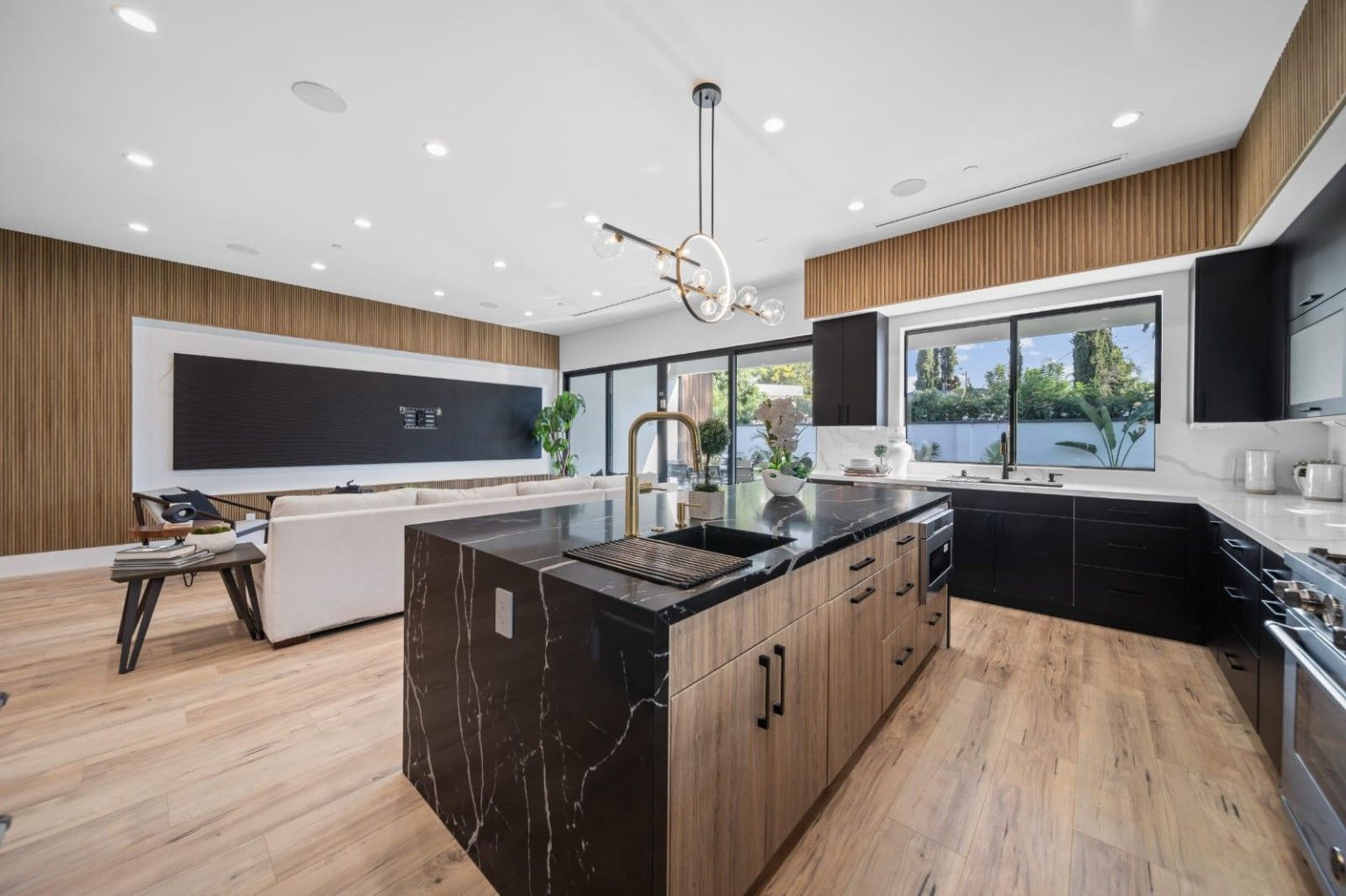 Connected kitchen and living space with warm wood, dark cabinetry and a large island