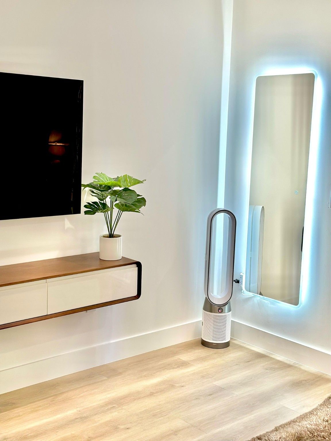Interior with a wall-mounted television, a floating console and a tall illuminated mirror