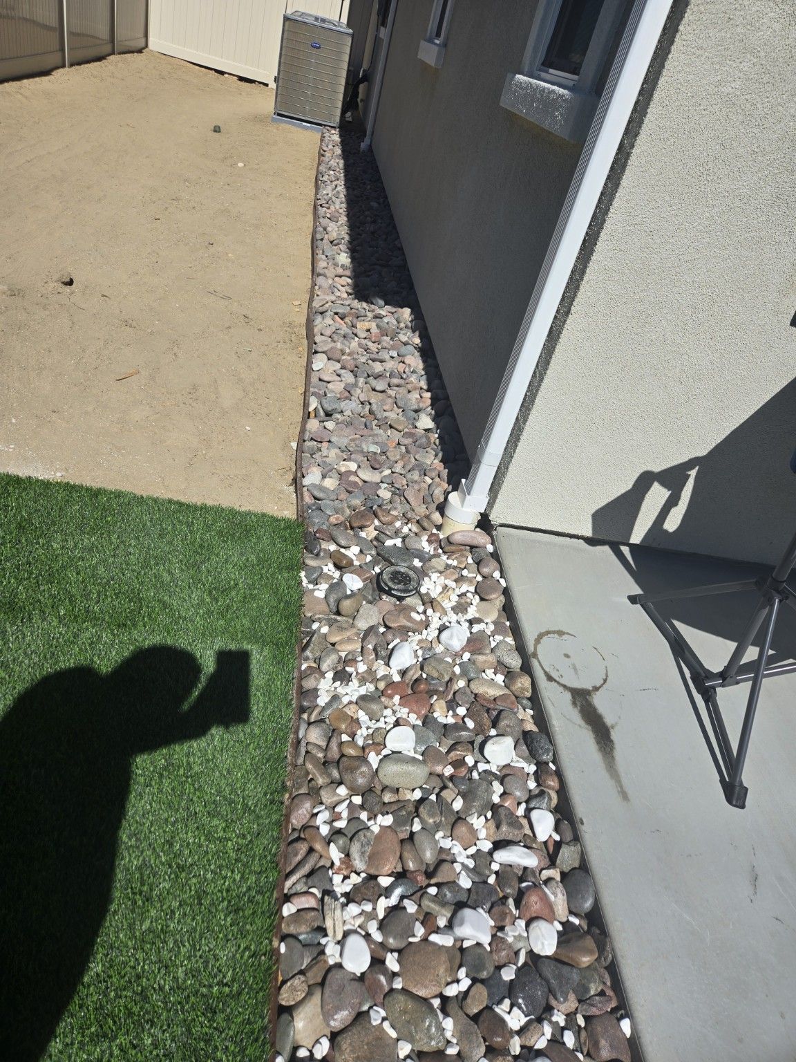 Close view of turf, a concrete path and a decorative rock border beside an exterior wall