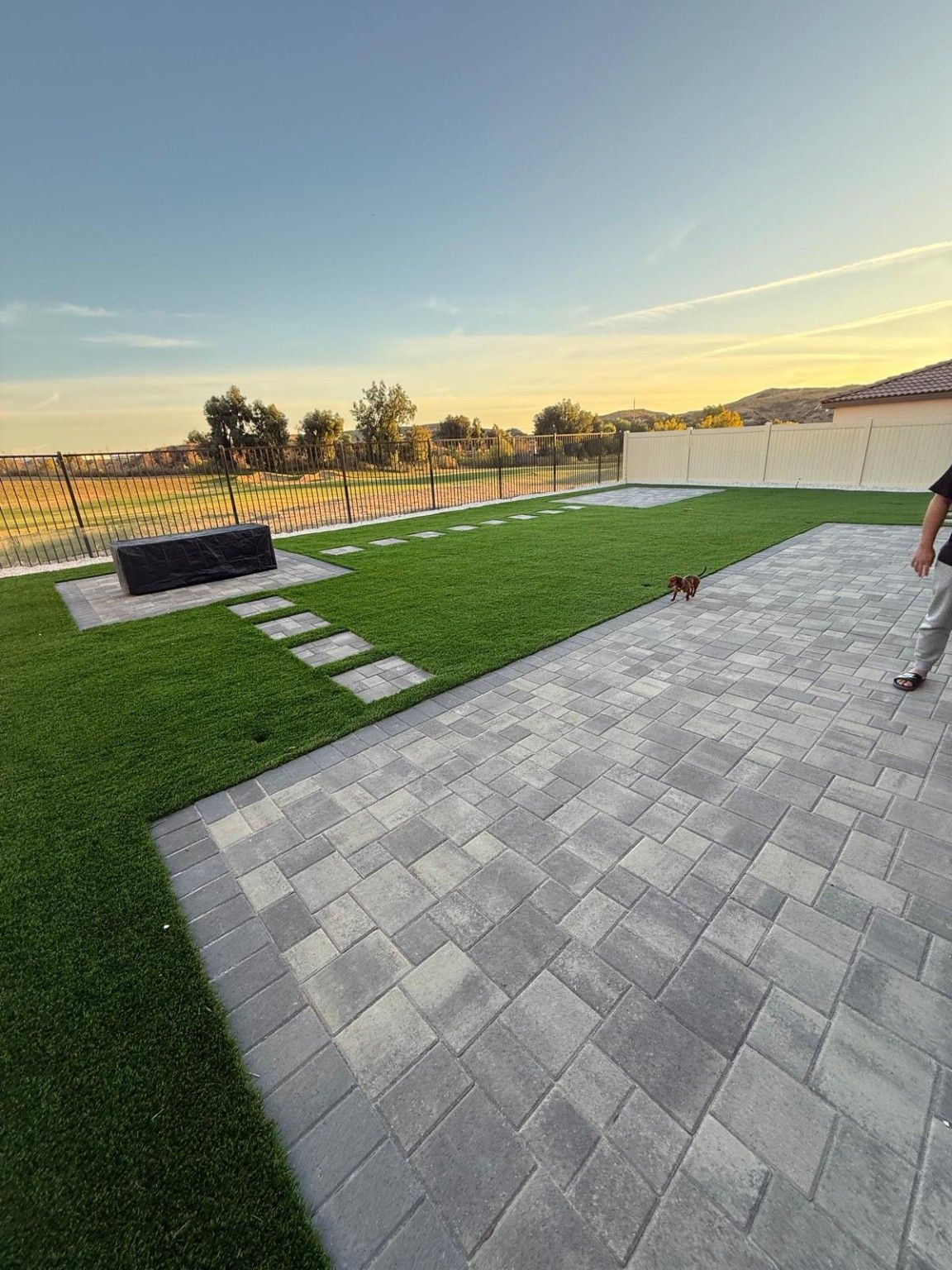 Wide view of gray paving beside artificial turf and fencing