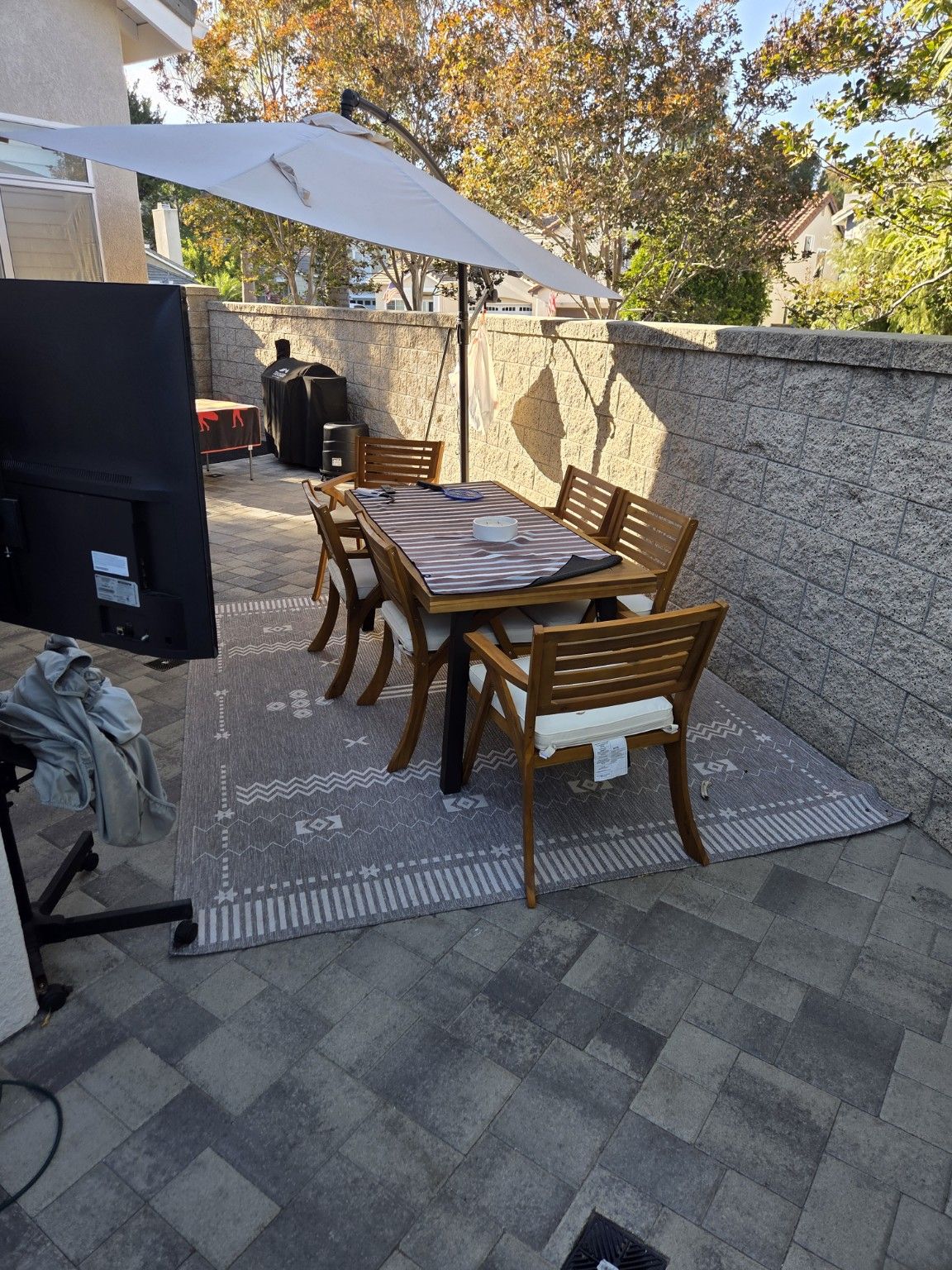Outdoor dining table and chairs on a gray paver patio beside a boundary wall
